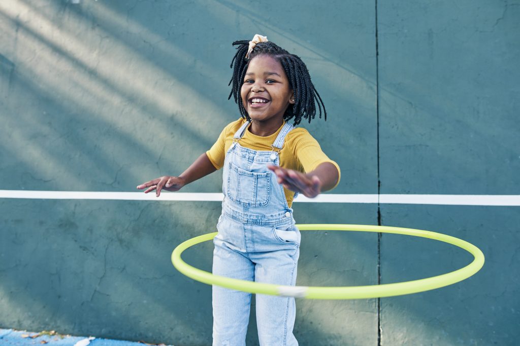 Happy, playing and portrait of a child with a hula hoop for fitness, practice and hobby. Smile, carefree and an African girl with a toy for happiness, playtime and break on a school playground