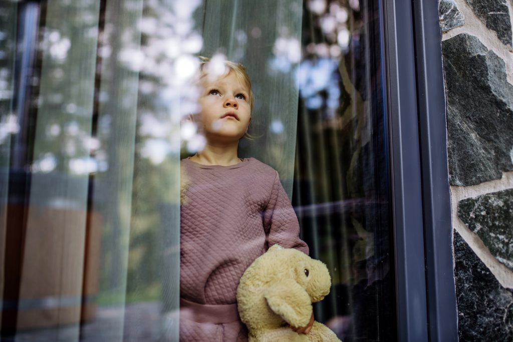 Little girl holding a teddy bear and looking out the window